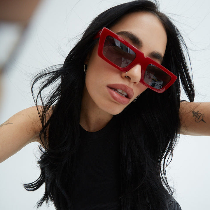 Lali wearing red sunglasses with a blurred background