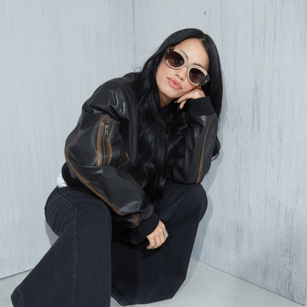 Lali wearing a black leather jacket and sunglasses against a light gray background