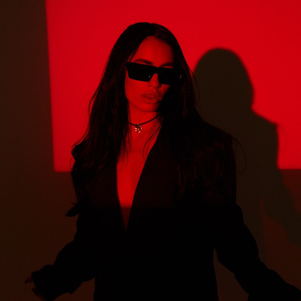 Lali wearing sunglasses and a dark outfit against a red background