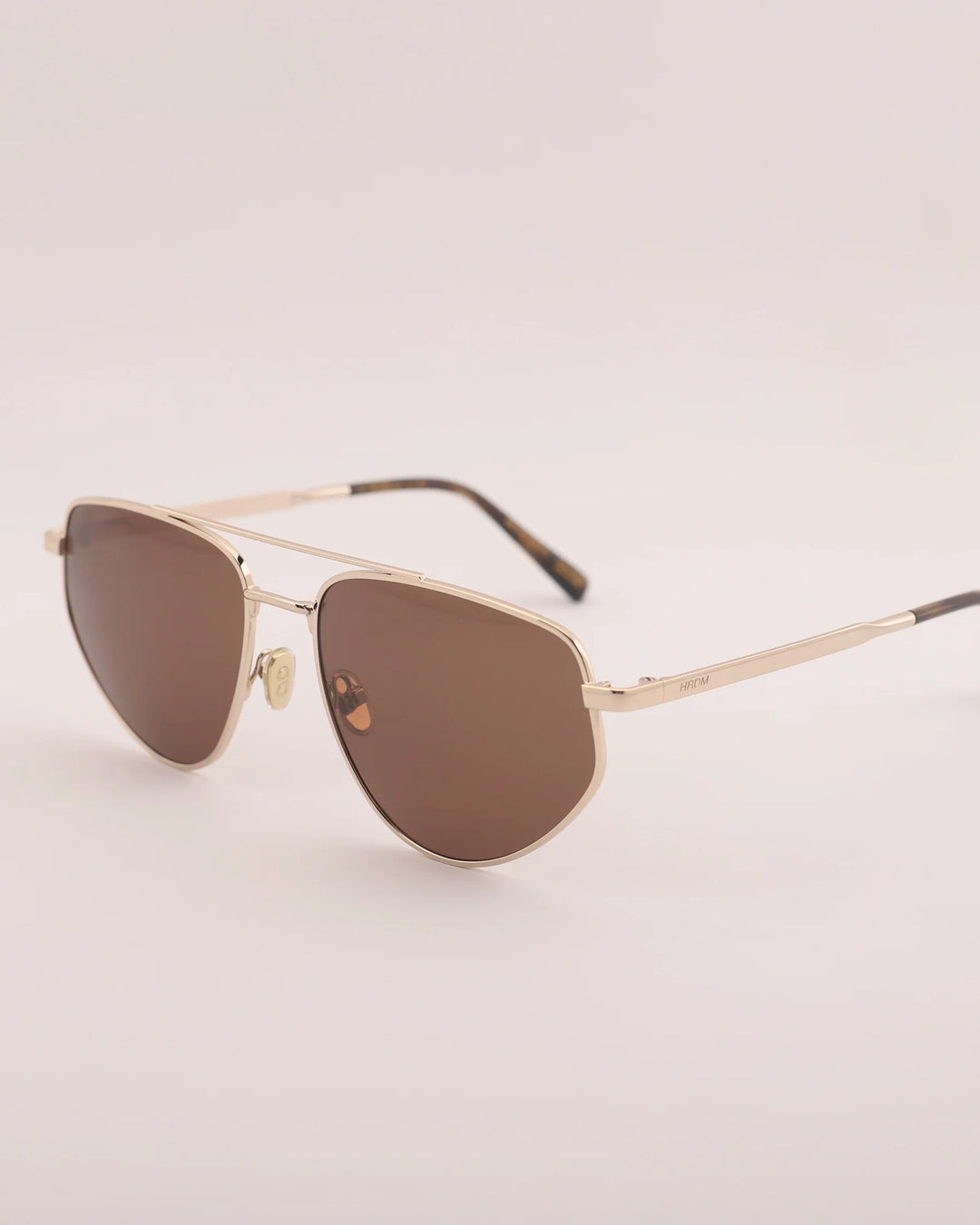 Gold-framed sunglasses with brown lenses on a light gray background