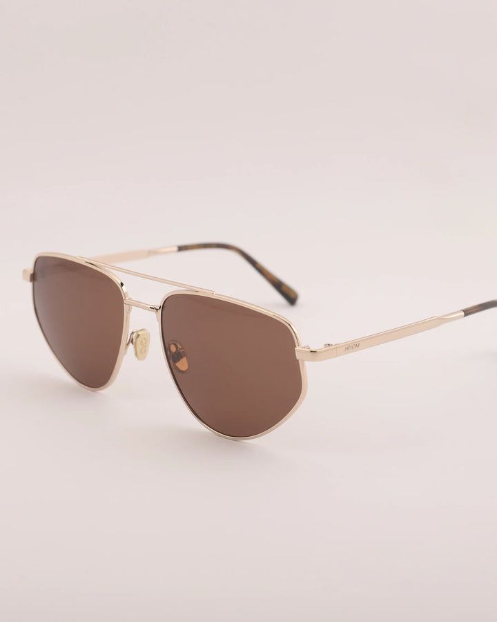 Gold-framed sunglasses with brown lenses on a light gray background