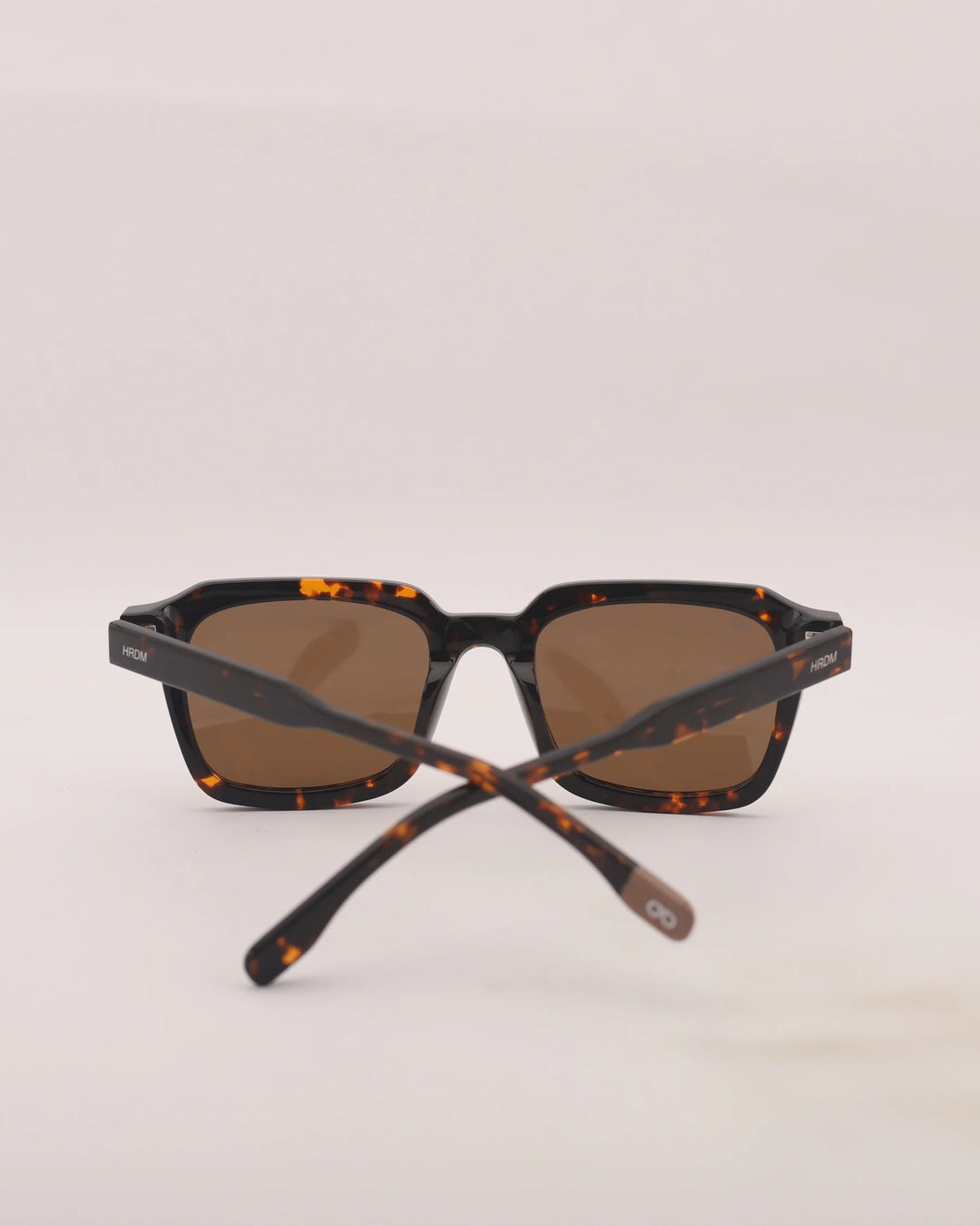 Sunglasses with tortoiseshell frame and brown lenses on a light gray background