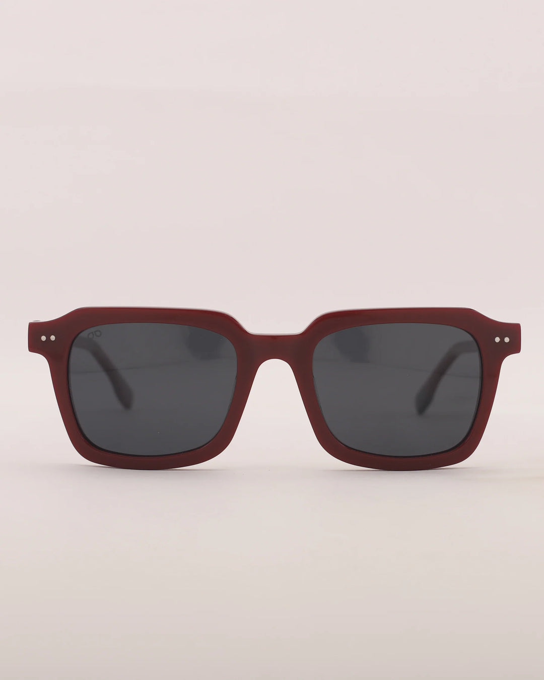 Sunglasses with a maroon frame and dark lenses on a light gray background