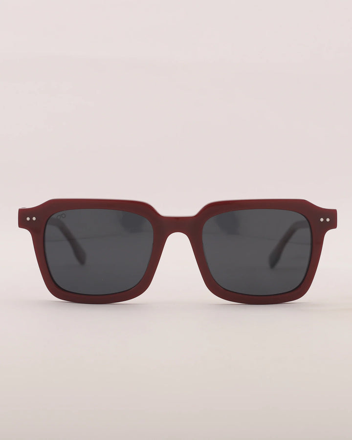 Sunglasses with a maroon frame and dark lenses on a light gray background