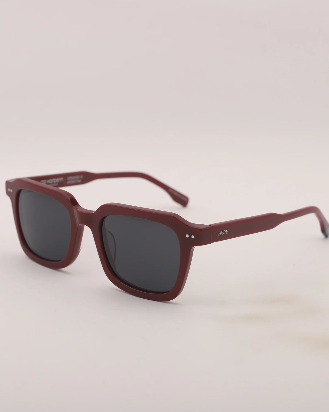 Maroon sunglasses with dark lenses on a light gray background