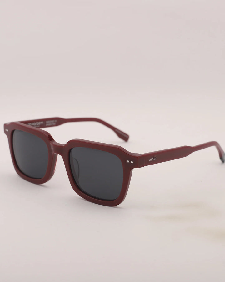 Maroon sunglasses with dark lenses on a light gray background