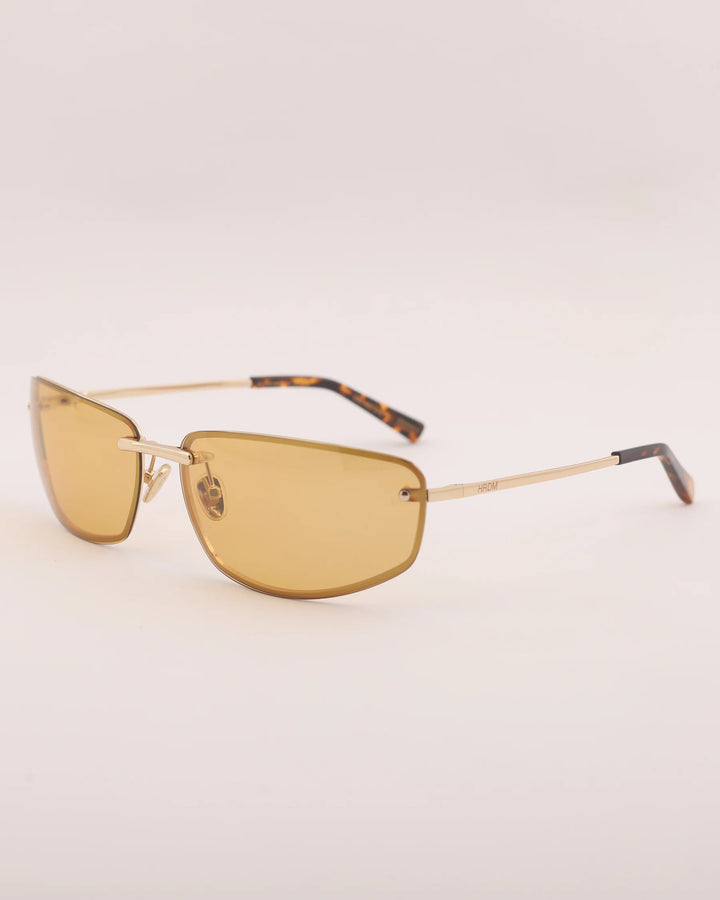Gold-framed sunglasses with amber lenses on a light beige background