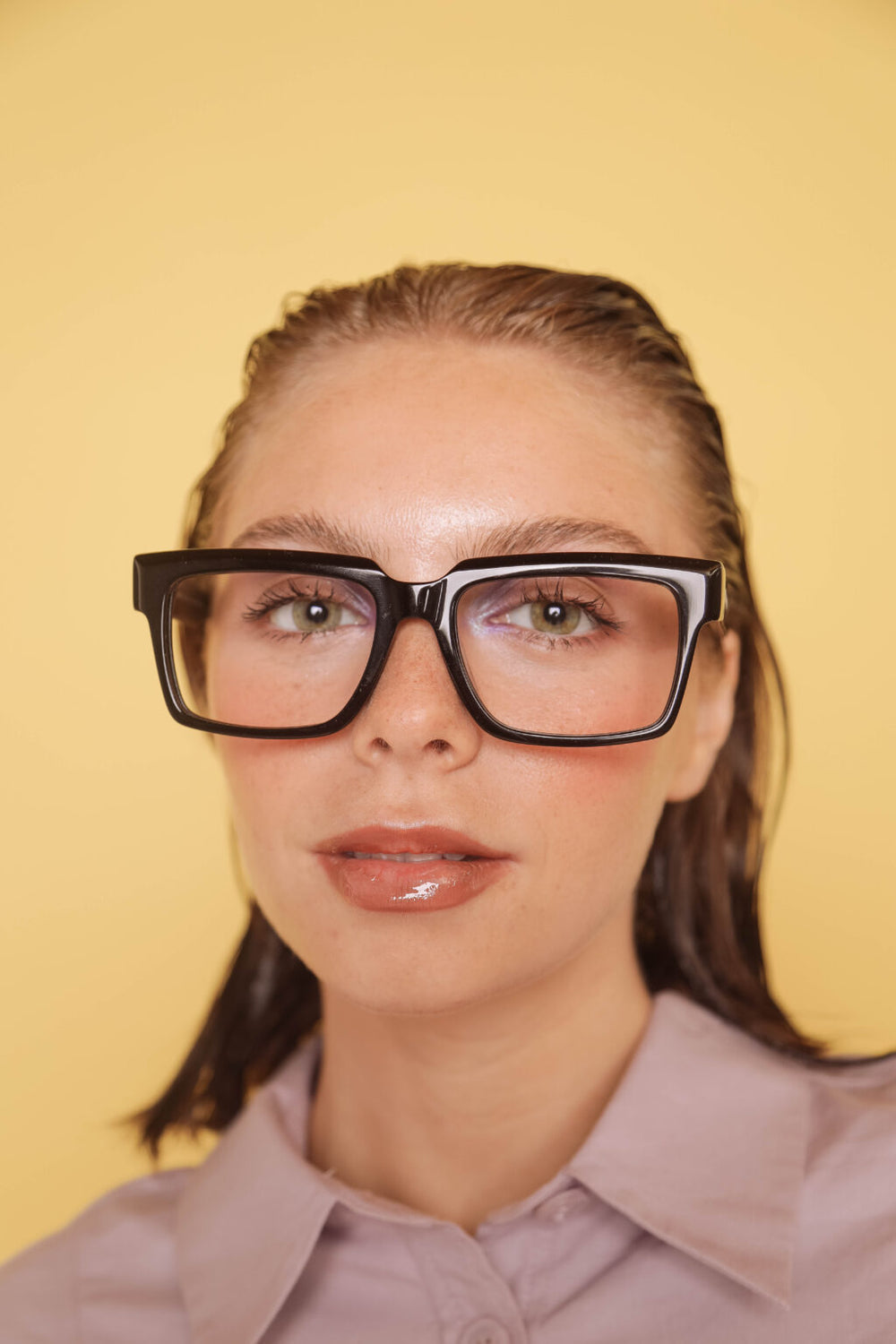 Woman wearing large black-framed glasses against a yellow background