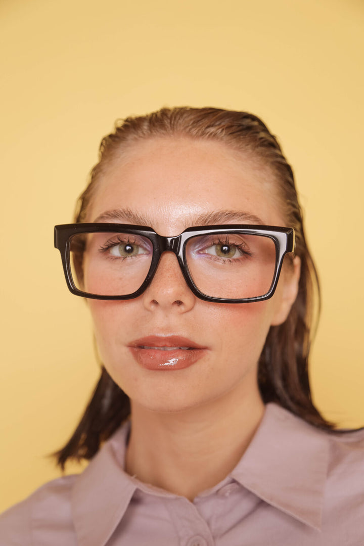 Woman wearing large black-framed glasses against a yellow background