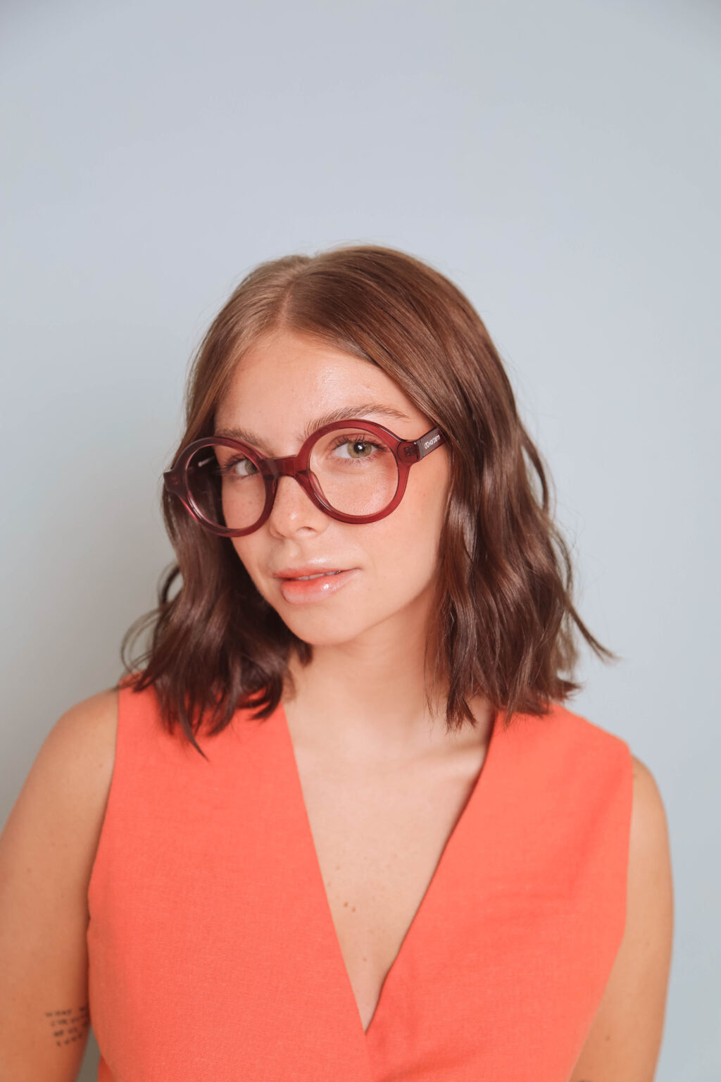 Woman wearing red glasses and an orange top against a light gray background