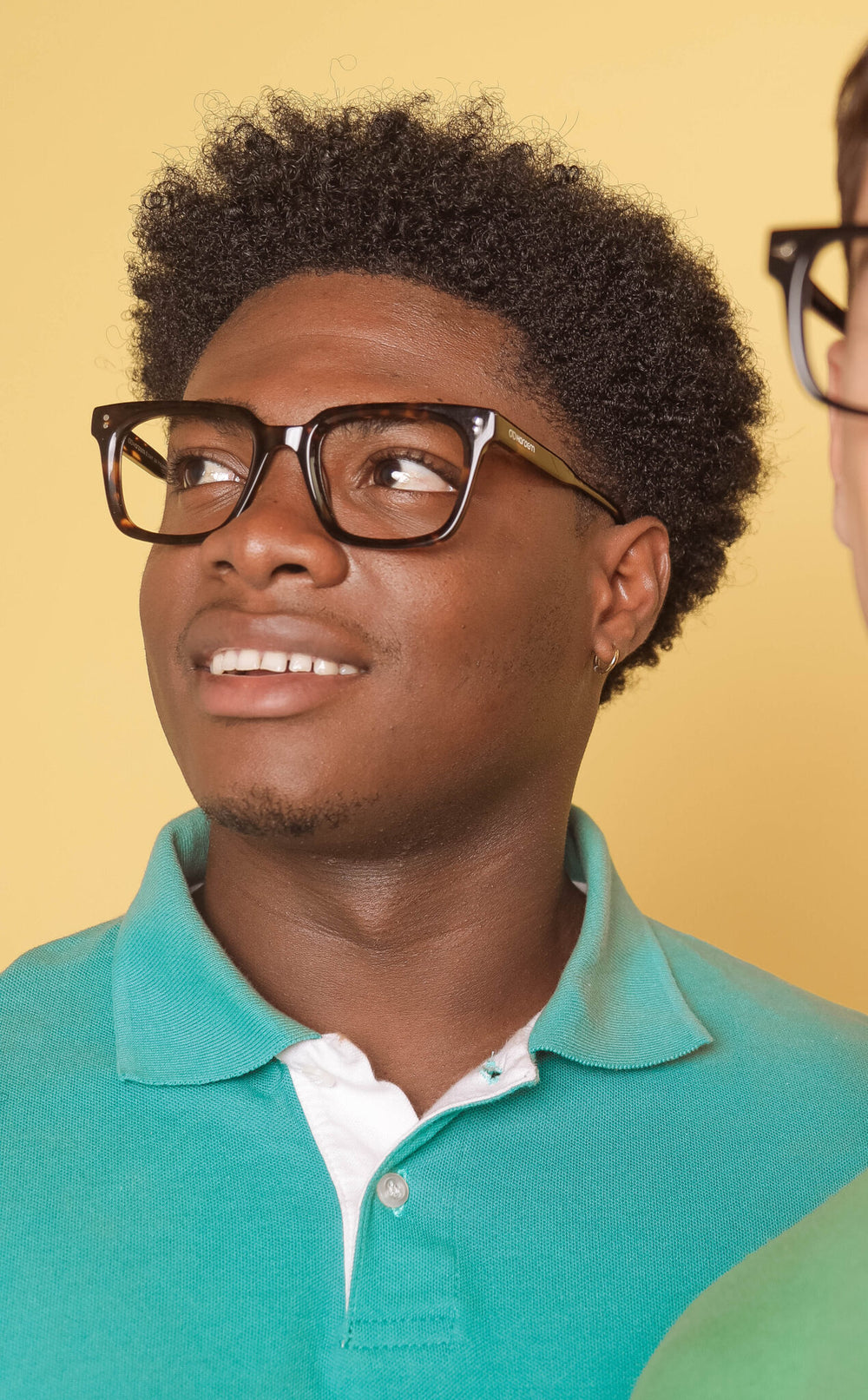 Man wearing glasses and a teal polo shirt against a yellow background