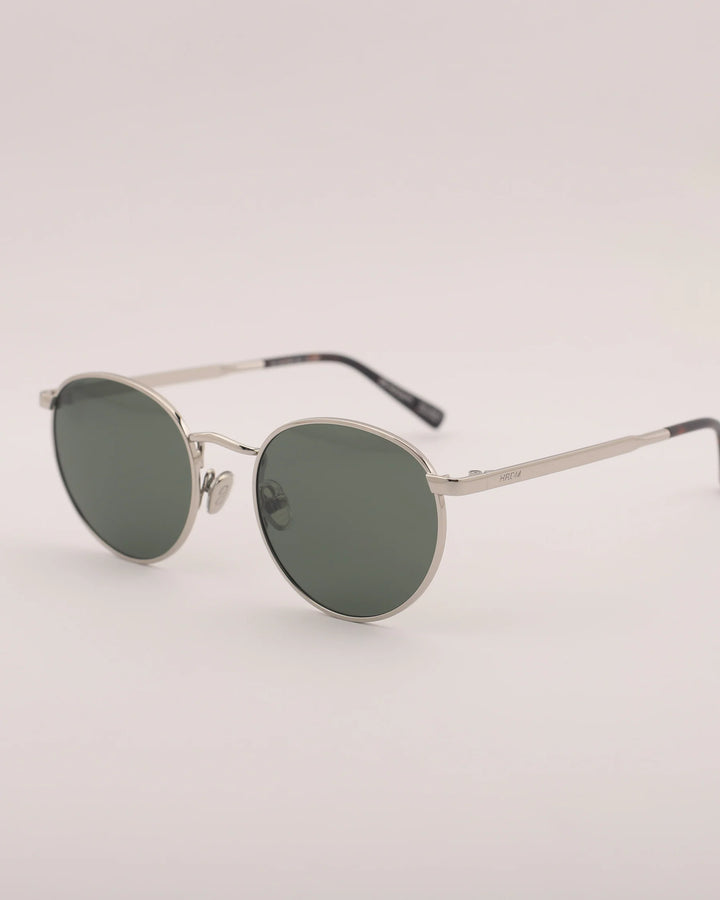 Round sunglasses with dark lenses and thin metal frame on a light gray background