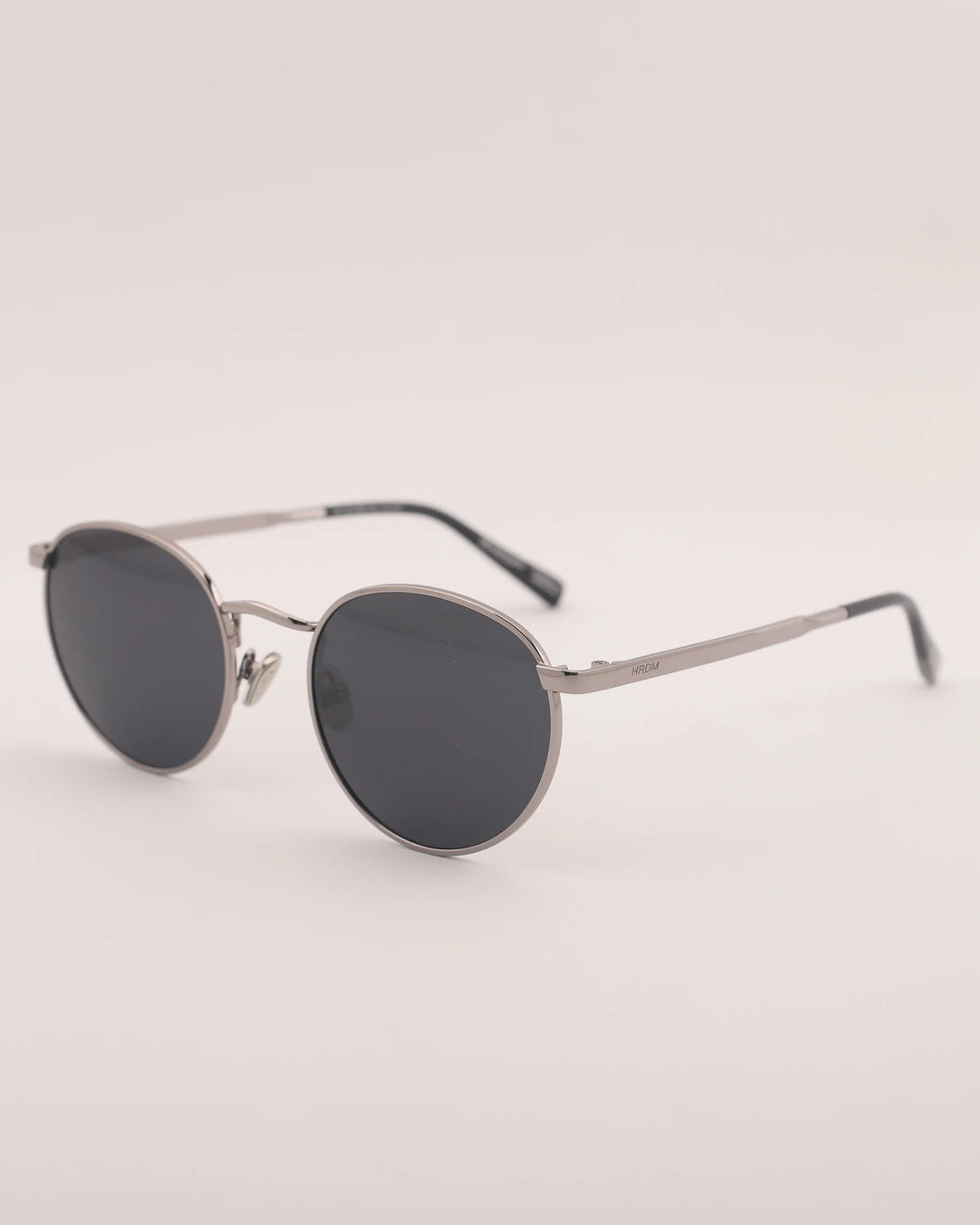 Round sunglasses with dark lenses and thin metal frame on a light gray background