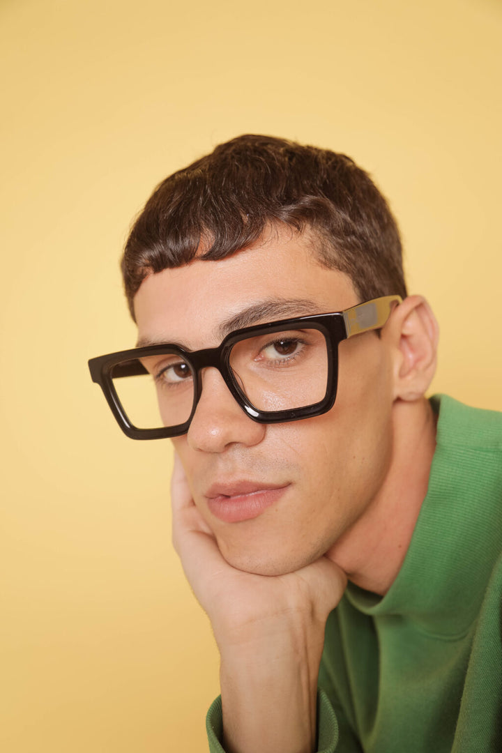 Person wearing black glasses with a yellow background