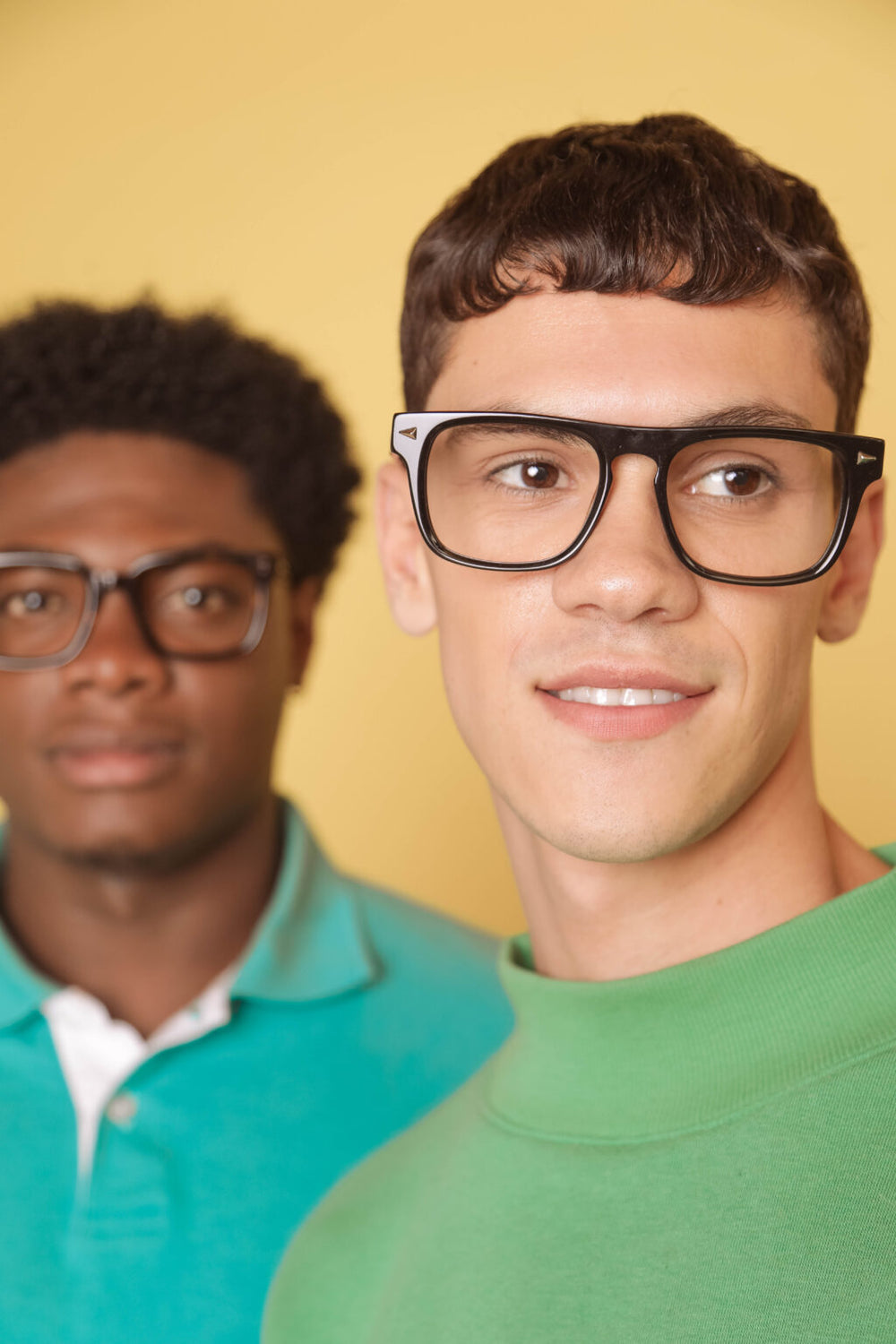 Two men wearing glasses with a yellow background