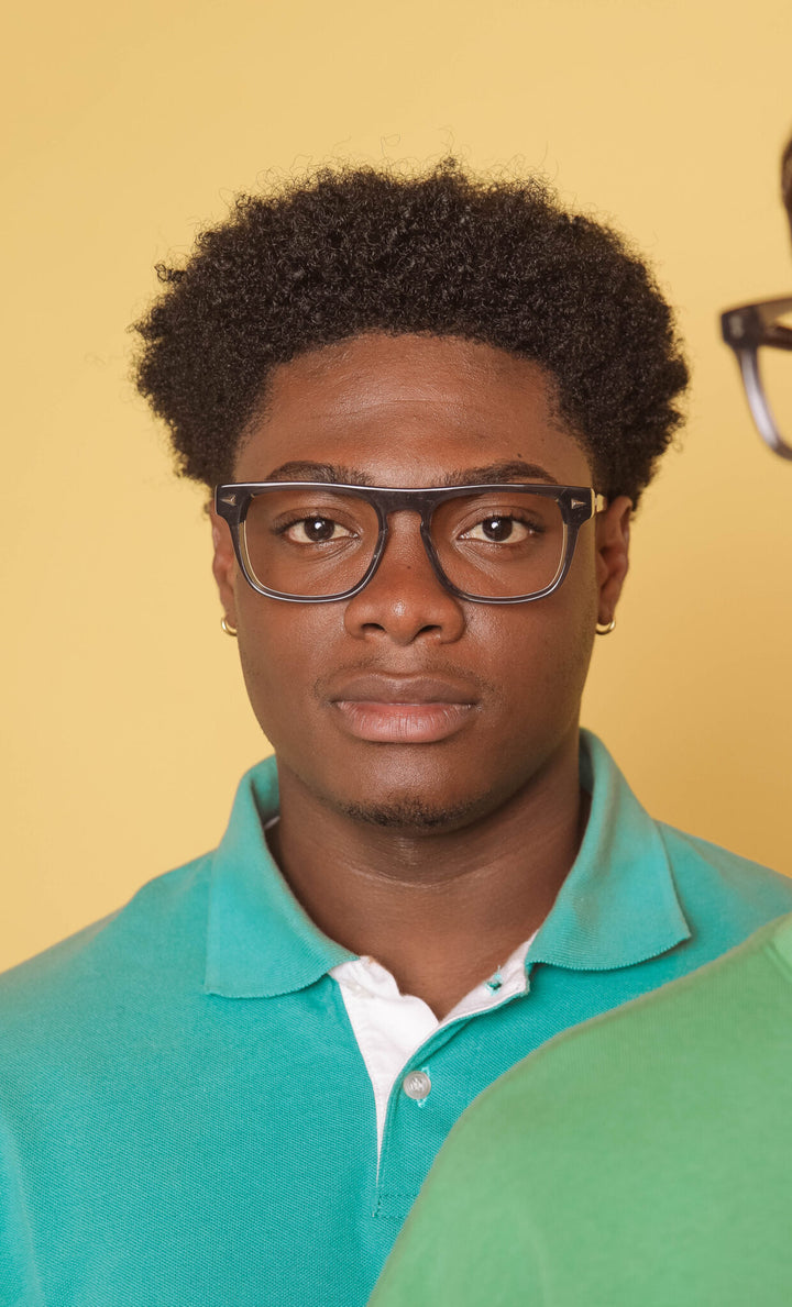 Man wearing glasses and a teal polo shirt against a beige background