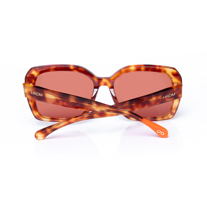 Sunglasses with tortoiseshell frame and red-tinted lenses on a white background