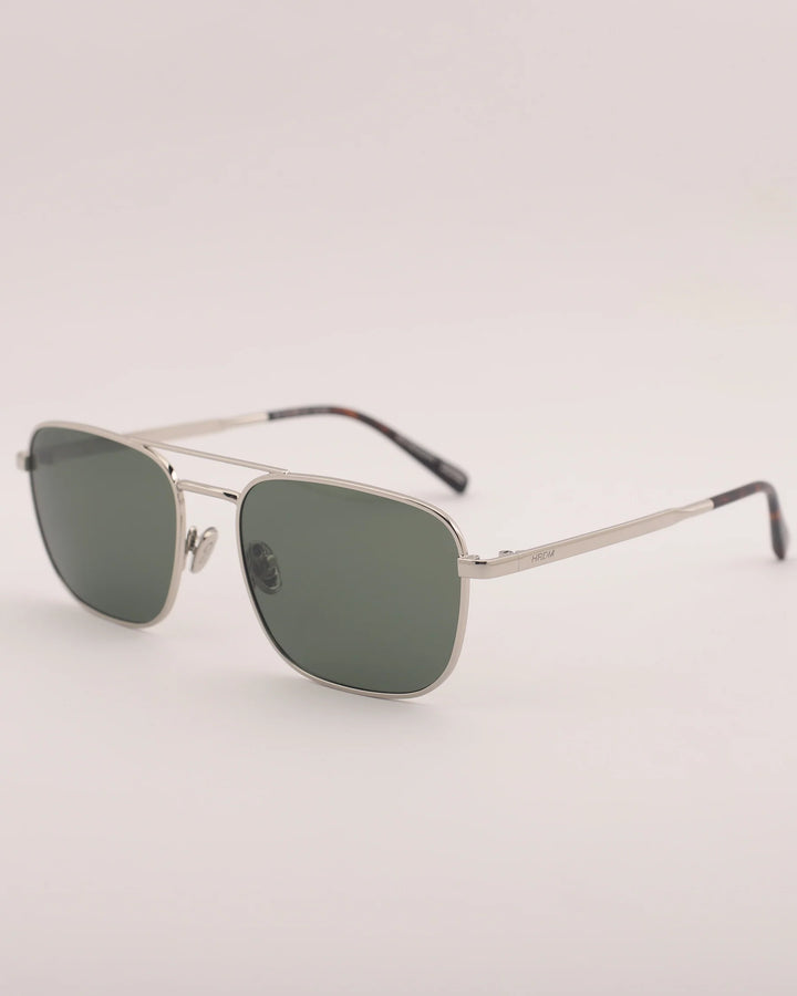 Sunglasses with silver frame and green lenses on a light gray background
