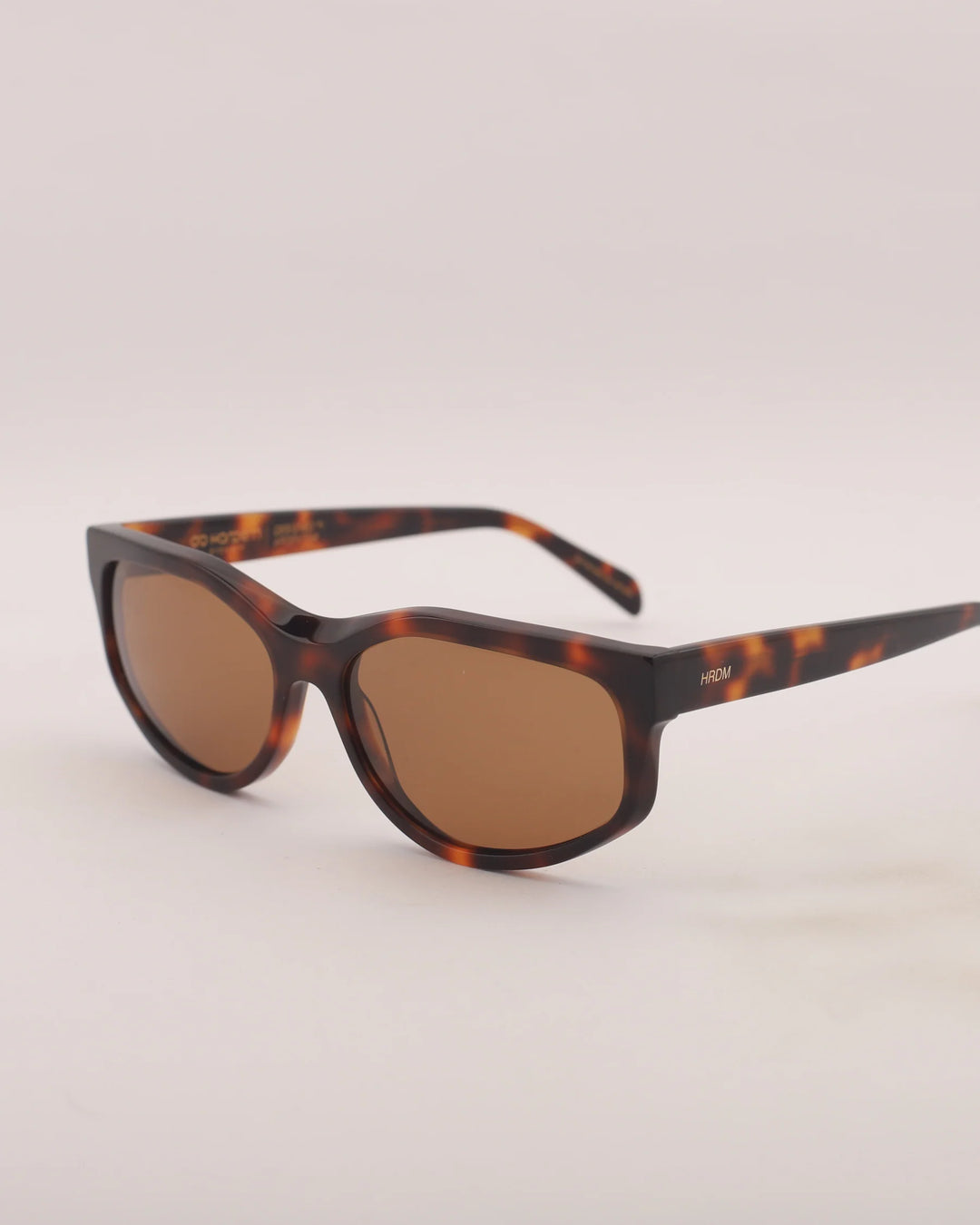 Sunglasses with tortoiseshell frame and brown lenses on a light gray background