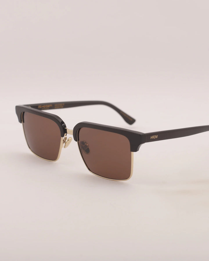 Black sunglasses with brown lenses on a light beige background
