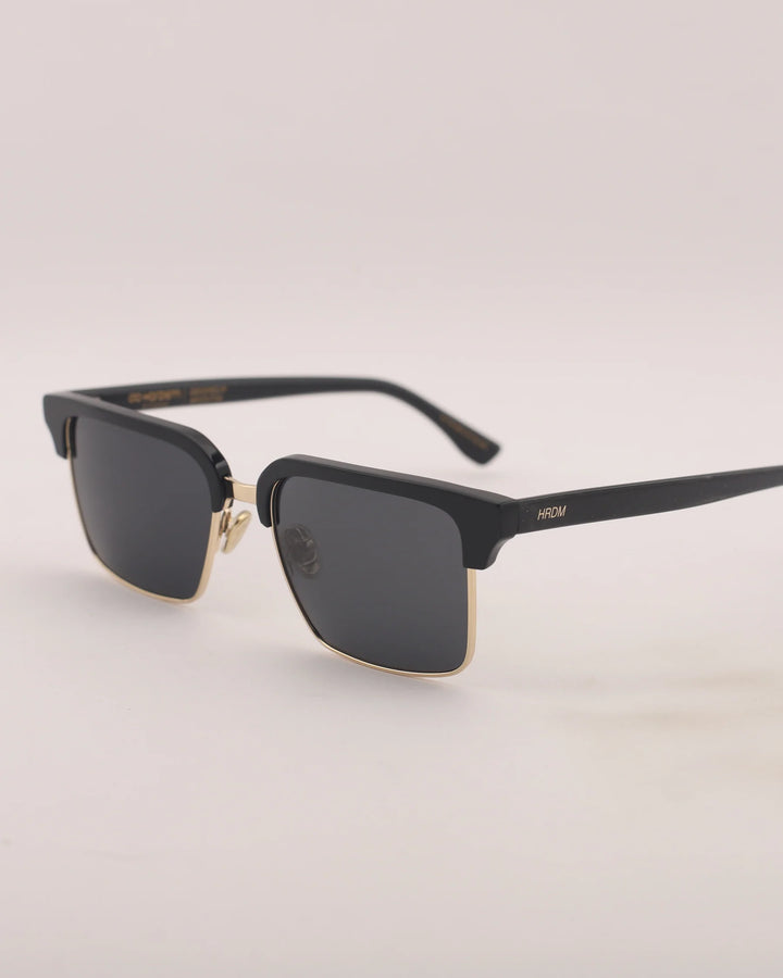Black sunglasses with gold accents on a light gray background