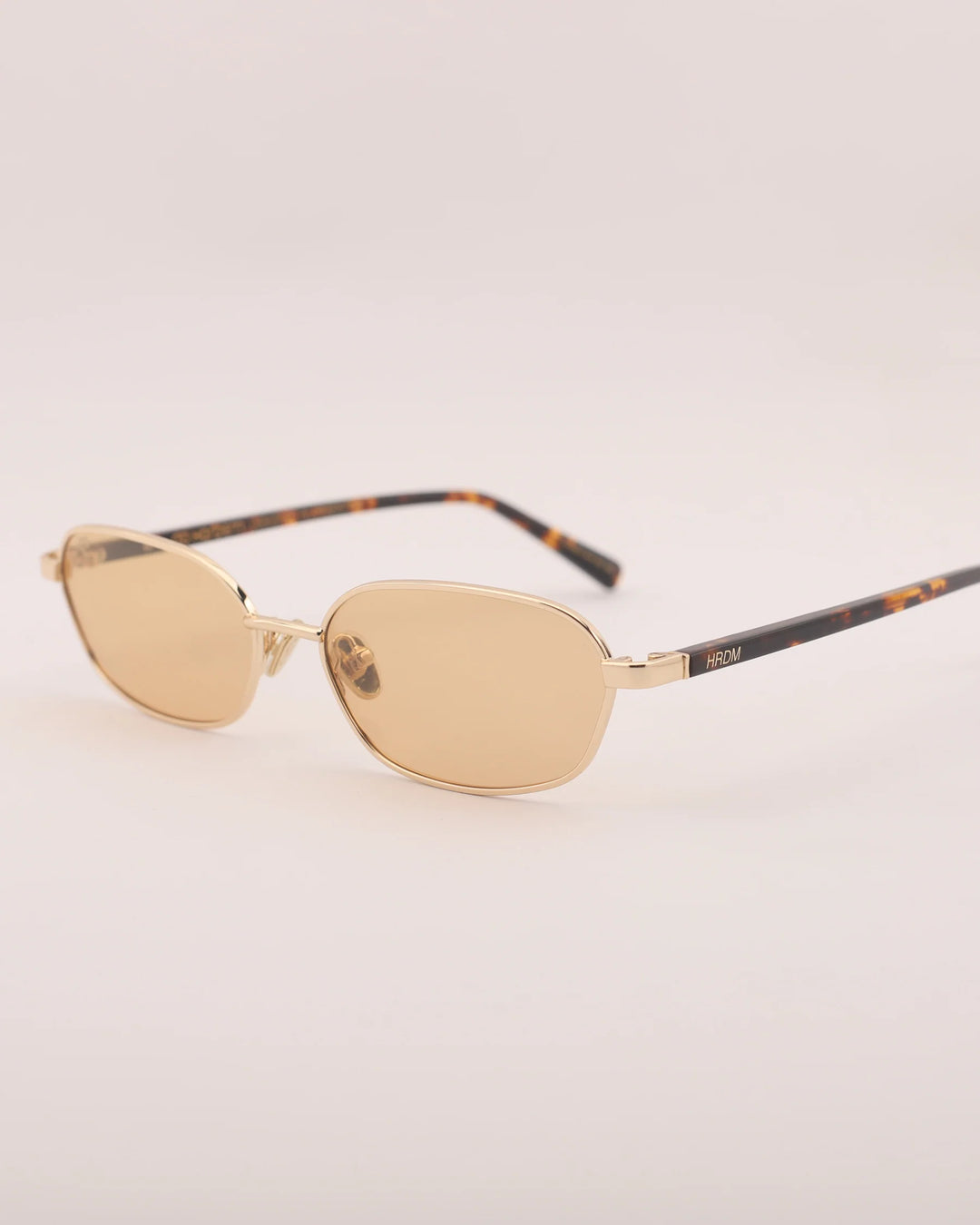 Gold sunglasses with tortoiseshell arms on a light gray background