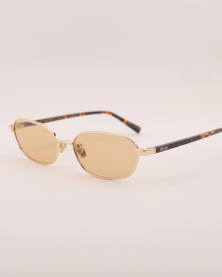 Gold sunglasses with tortoiseshell arms on a light gray background