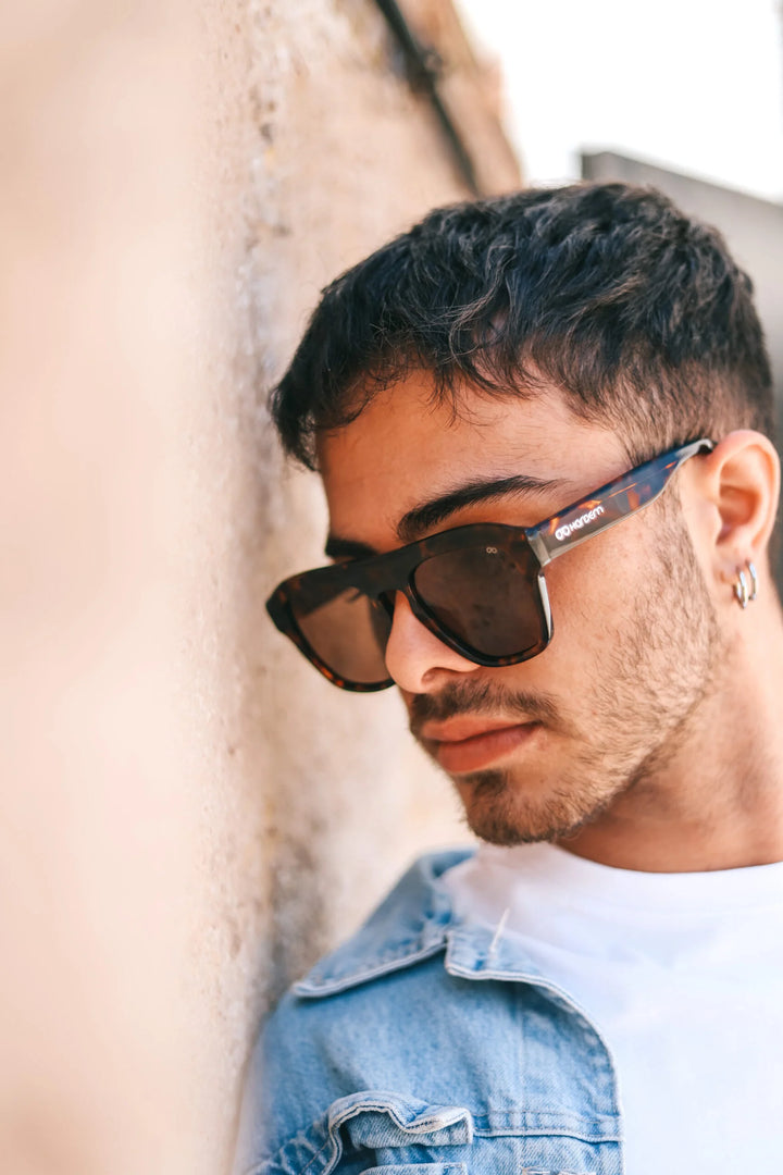 Man wearing sunglasses and a denim jacket against a neutral background