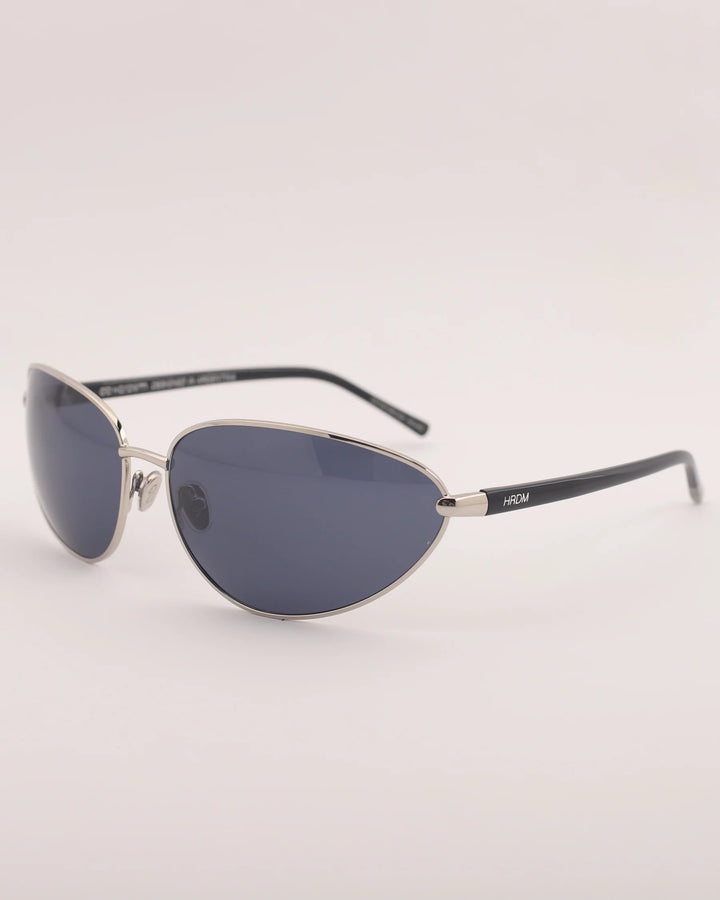 Sunglasses with a silver frame and dark lenses on a light gray background